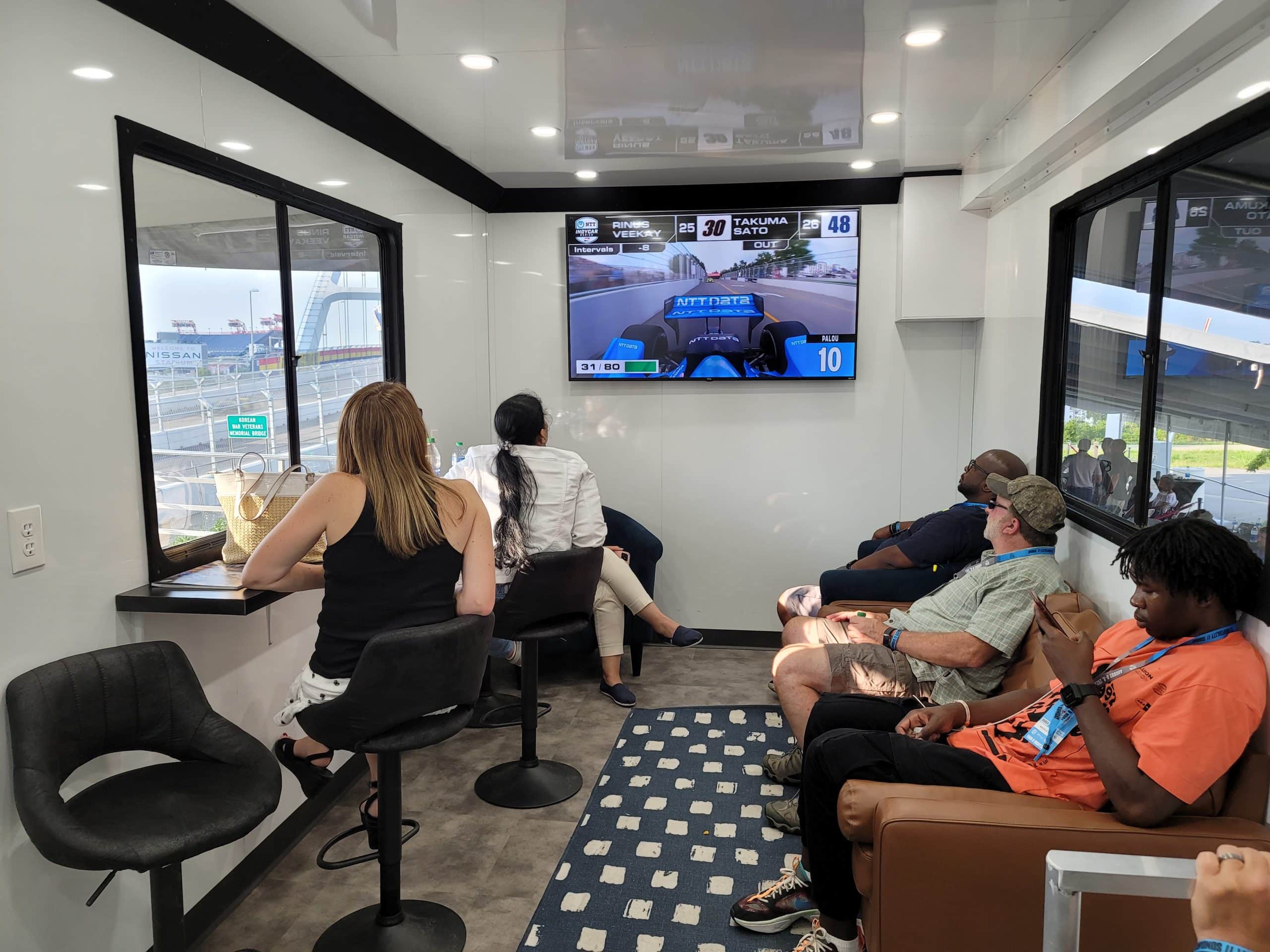 Interior of trailer at Music City Grand Prix with people sitting and watching TV