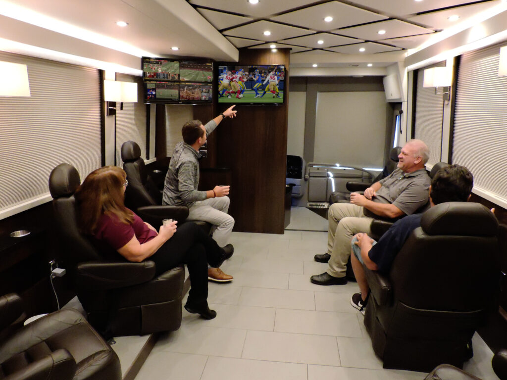 Interior of custom bus designed by Brewco with people sitting inside while watching TV