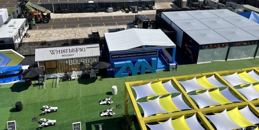 An aerial view of a sprawling outdoor area filled with numerous yellow and blue tents, hosting the grand activation at the Formula 1 Miami Grand Prix.